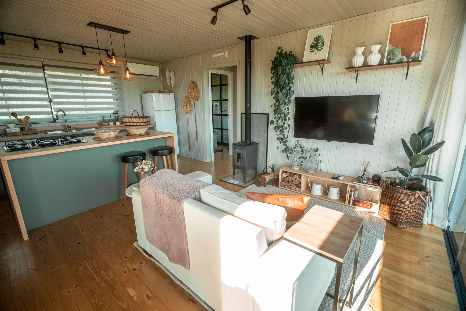 Sala de estar e cozinha modernas em conceito aberto, com piso de madeira, sofá, TV de parede, lareira e decoração.