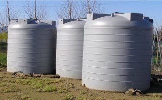 Tre grandi serbatoi cilindrici grigi per l'acqua all'aperto, sull'erba.