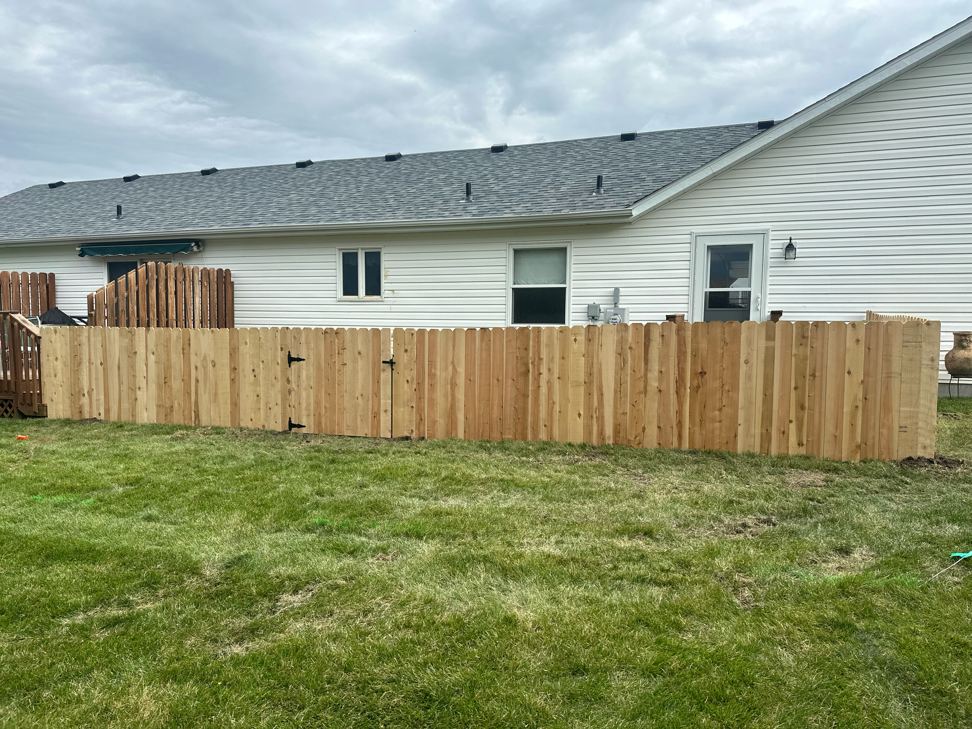 Wooden fence in a grassy backyard, bordering a white house with a gray roof.