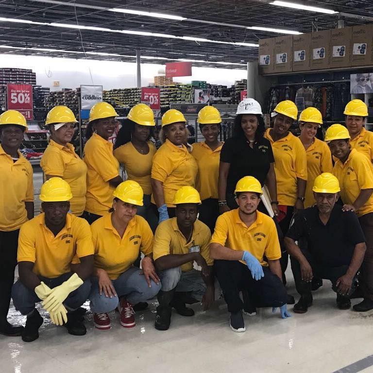 Group of people in yellow hard hats and shirts pose in a store. Some crouch or kneel.