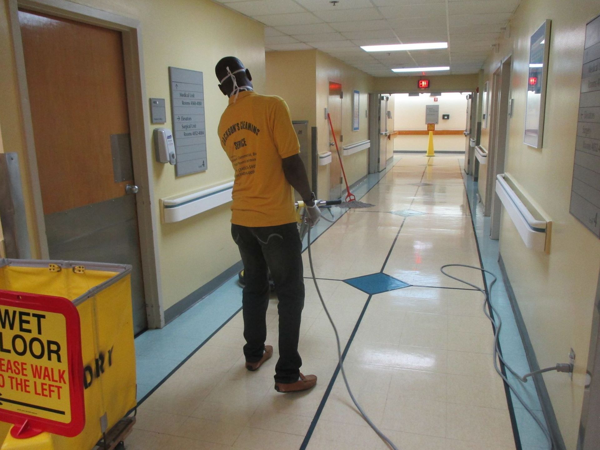 Person cleaning a hospital hallway with a machine, near a