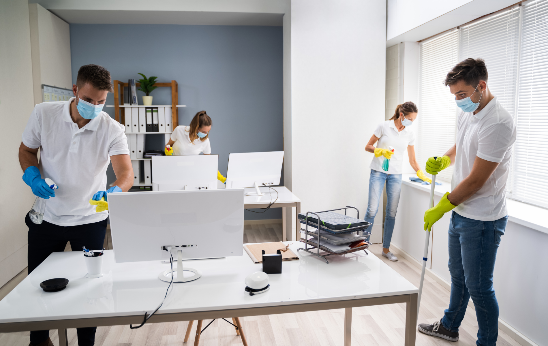 Office cleaners wearing masks and gloves sanitize desks and windows.