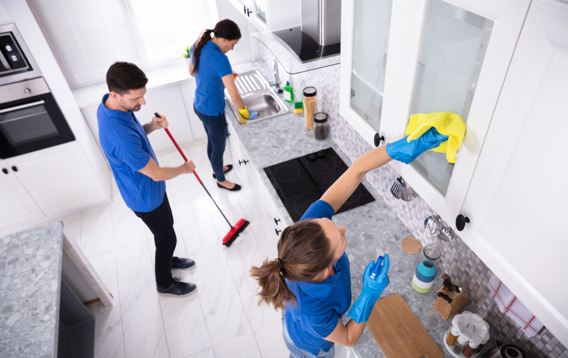 Professional cleaners in white polo shirts, masks, and gloves sanitize a bright office workspace.
