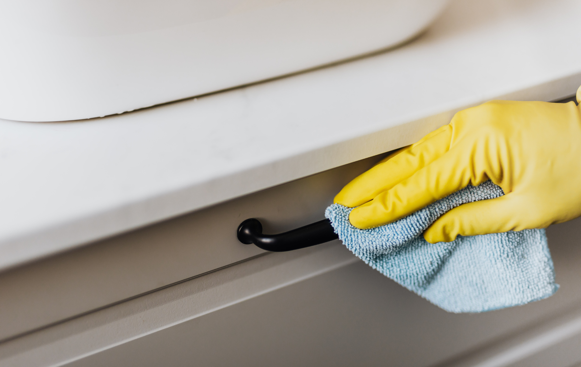 Hand in yellow glove cleaning black drawer handle with a blue cloth.