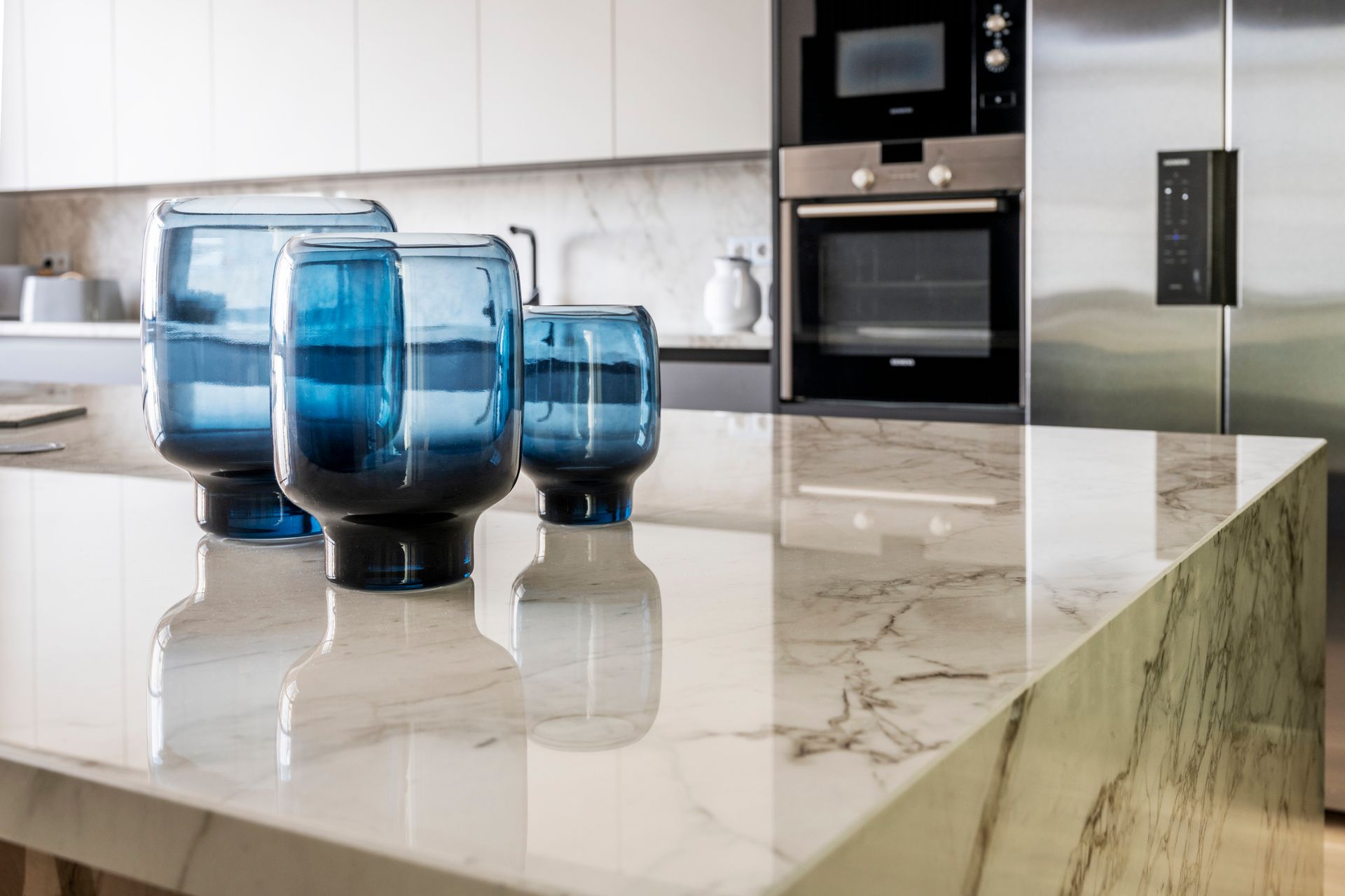 Marble island detail of a large kitchen with stainless steel appliances and blue glass vases.