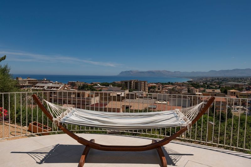 Terrazza sul tetto con sedie e tavoli color verde acqua con vista sul mare e sulla città costiera sotto un cielo azzurro.