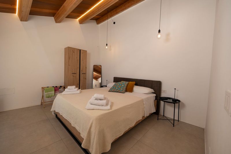 Camera da letto con porte finestre che si aprono sul balcone, con vista soleggiata sul mare e sul cielo azzurro.