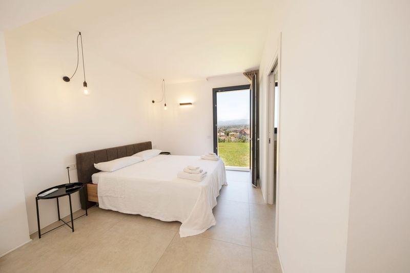 Camera da letto minimalista con letto bianco, testiera nera, tende trasparenti e piccoli comodini.