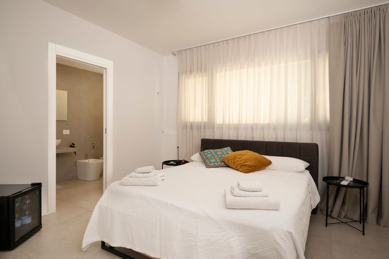 Camera da letto minimalista con letto in legno, lenzuola bianche e un'ampia finestra sopra la testiera.