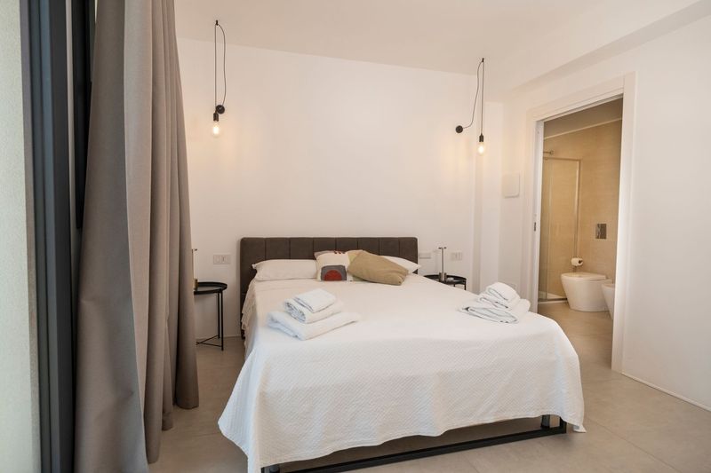 Camera da letto minimalista con divano grigio, letto matrimoniale e valigia sul pavimento.