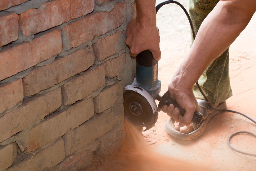 Person Using an Angle Grinder to Cut Into a Brick Wall — Ultra Services Ground Pavement & Building in Abercrombie, NSW