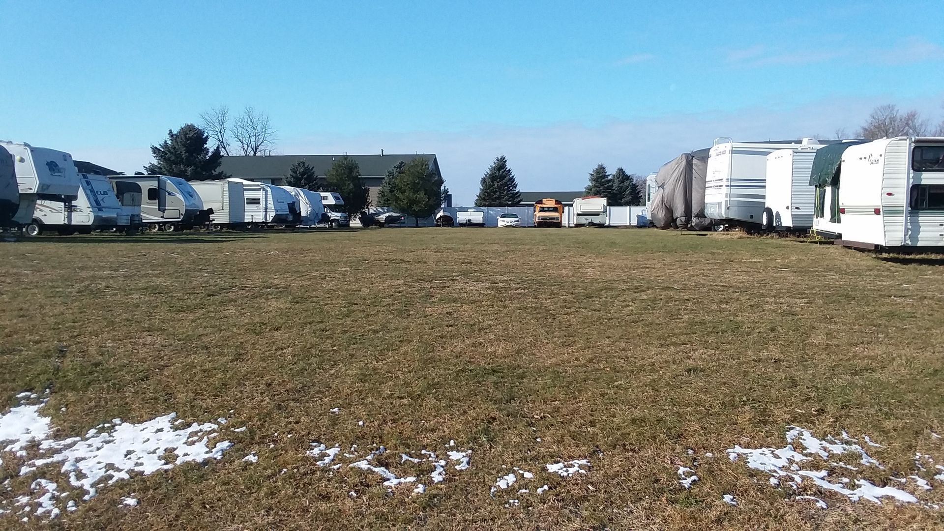 A row of rvs are parked in a grassy field