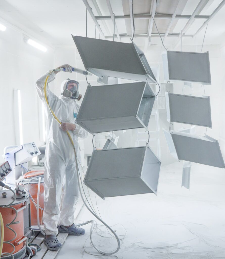 Person in a hazmat suit powder-coating a metal structure in a spray booth.