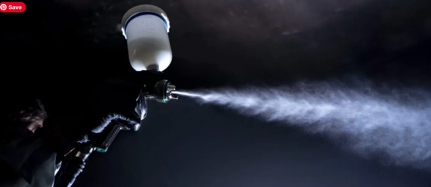 A person sprays paint from a sprayer in a dark setting, creating a misty spray.