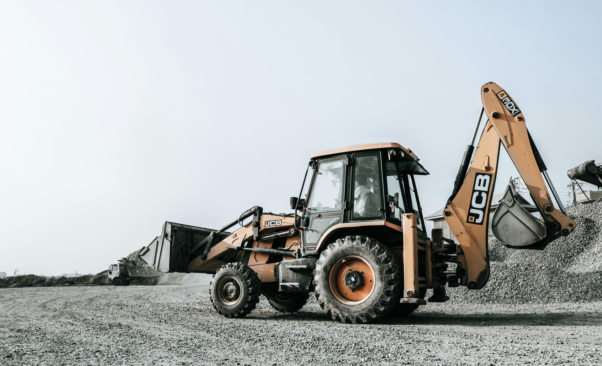 Yellow JCB backhoe loader on a gravel lot, scooping up material with its bucket.