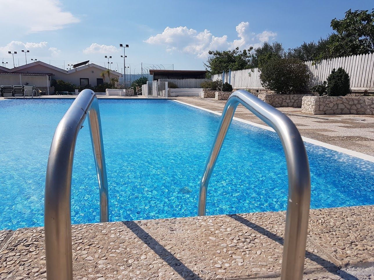 Piscina con scaletta in acciaio inox e acqua cristallina in una giornata di sole.