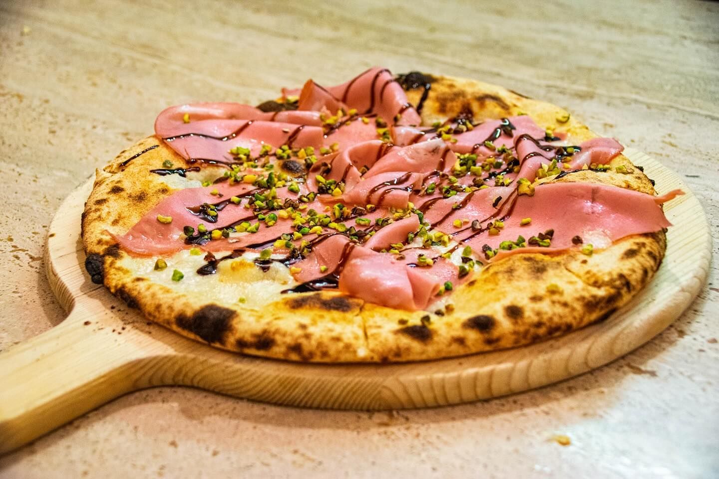 Pizza cotta nel forno a legna con prosciutto, erbe aromatiche e salsa di pomodoro, su una pala di legno.