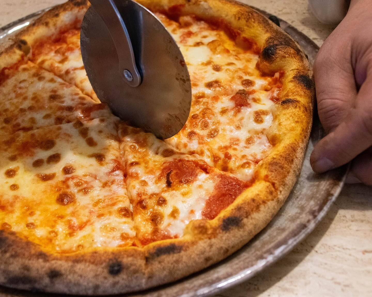 La pizza viene affettata con una rotella metallica su un vassoio, con una mano che tiene la crosta.