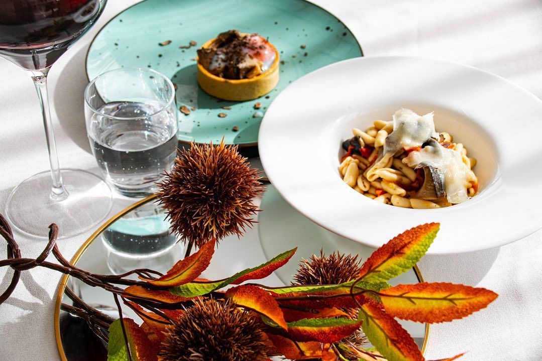 Antipasti gourmet serviti su un tavolo bianco con foglie decorative e un bicchiere d'acqua.