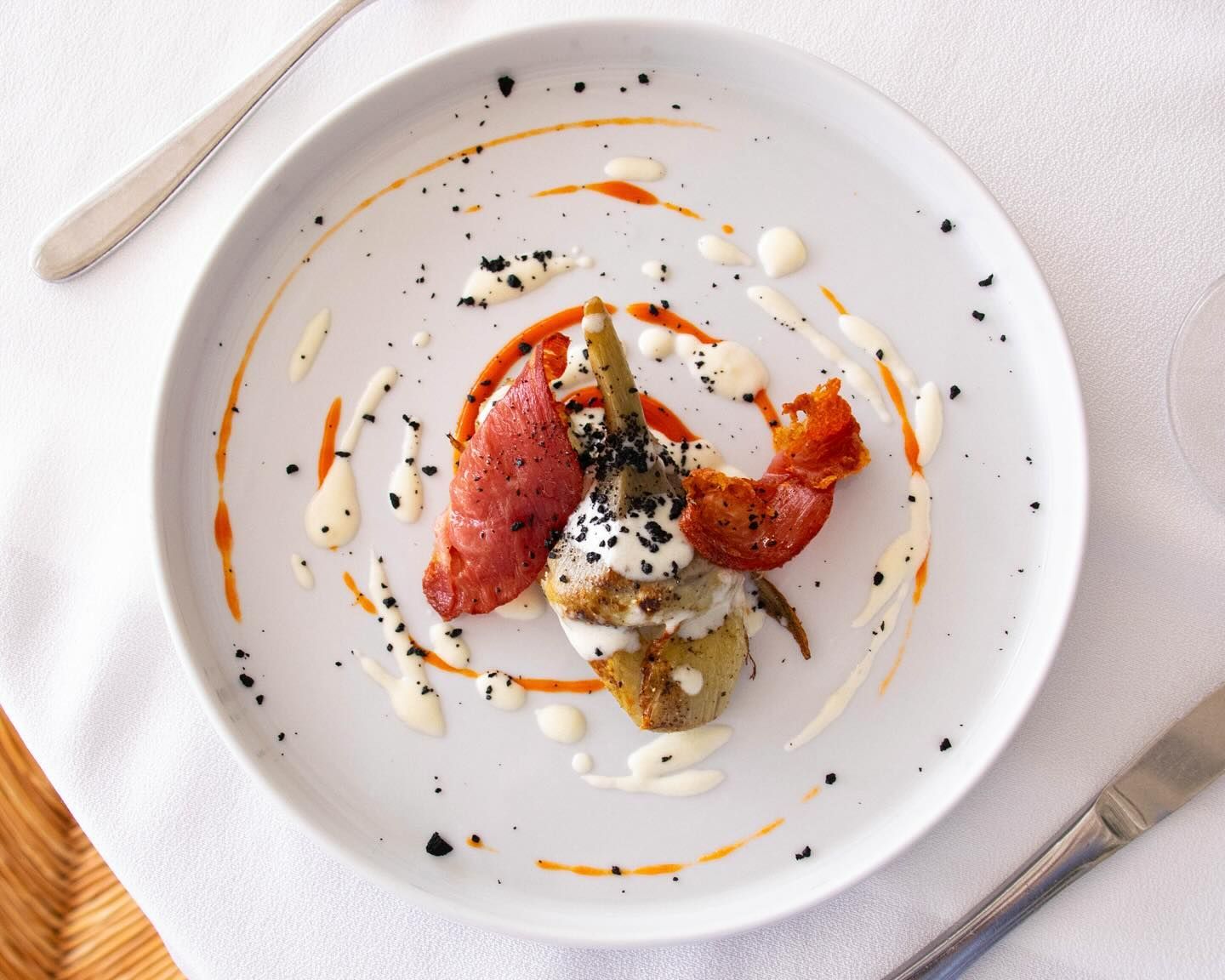 Dessert minimalista con frutti rossi, salsa di panna e semi di papavero su un piatto bianco.