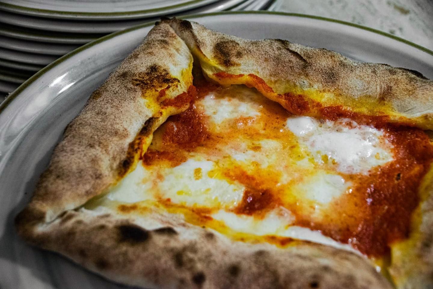 Pizza margherita rettangolare su un piatto, con formaggio fuso e bordi della crosta leggermente bruciacchiati.