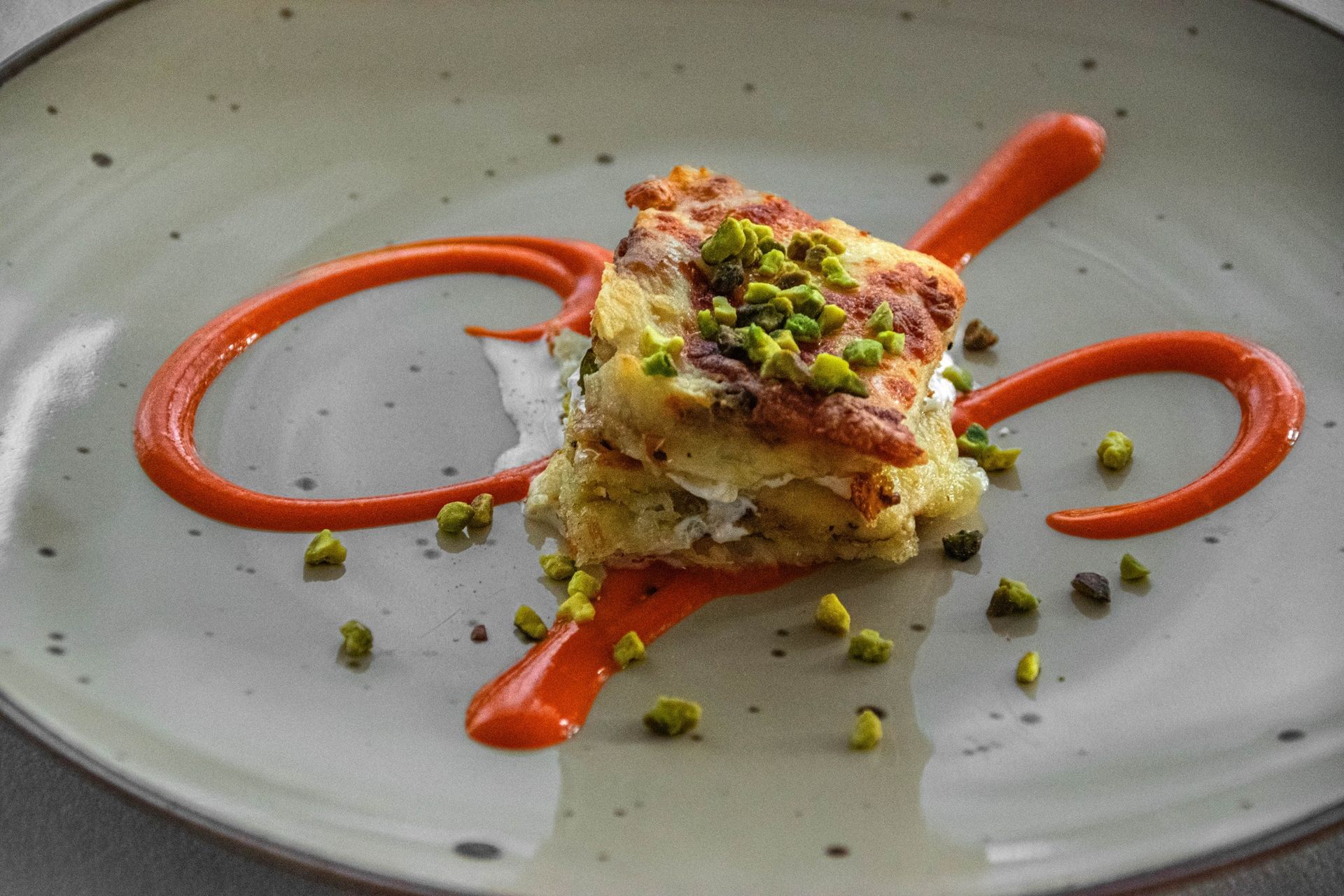 Quadratino da dessert con pistacchi e salsa all'arancia su un piatto grigio.