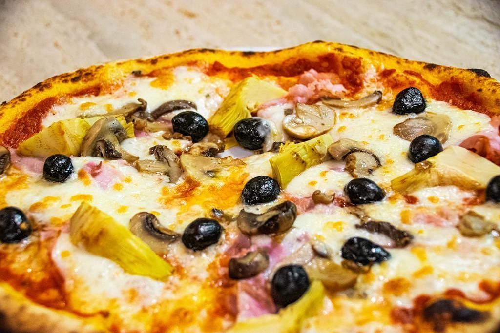 Primo piano di una pizza cotta al forno condita con olive nere, funghi e peperoni gialli.