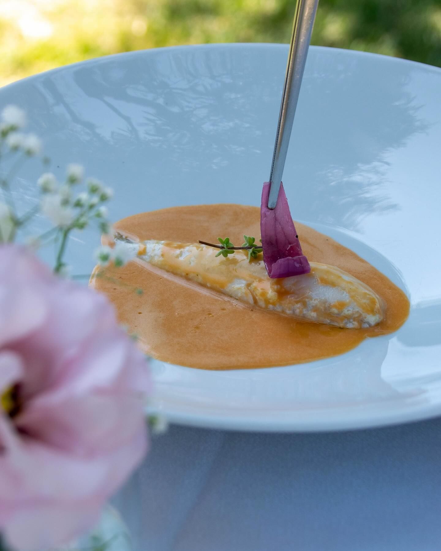 Dessert impiattato con salsa all'arancia e guarnizione viola, servito con un cucchiaio su un piatto bianco.