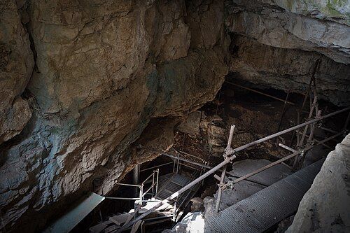 Una scala e una ringhiera metallica scendono in una grotta buia con pareti rocciose.