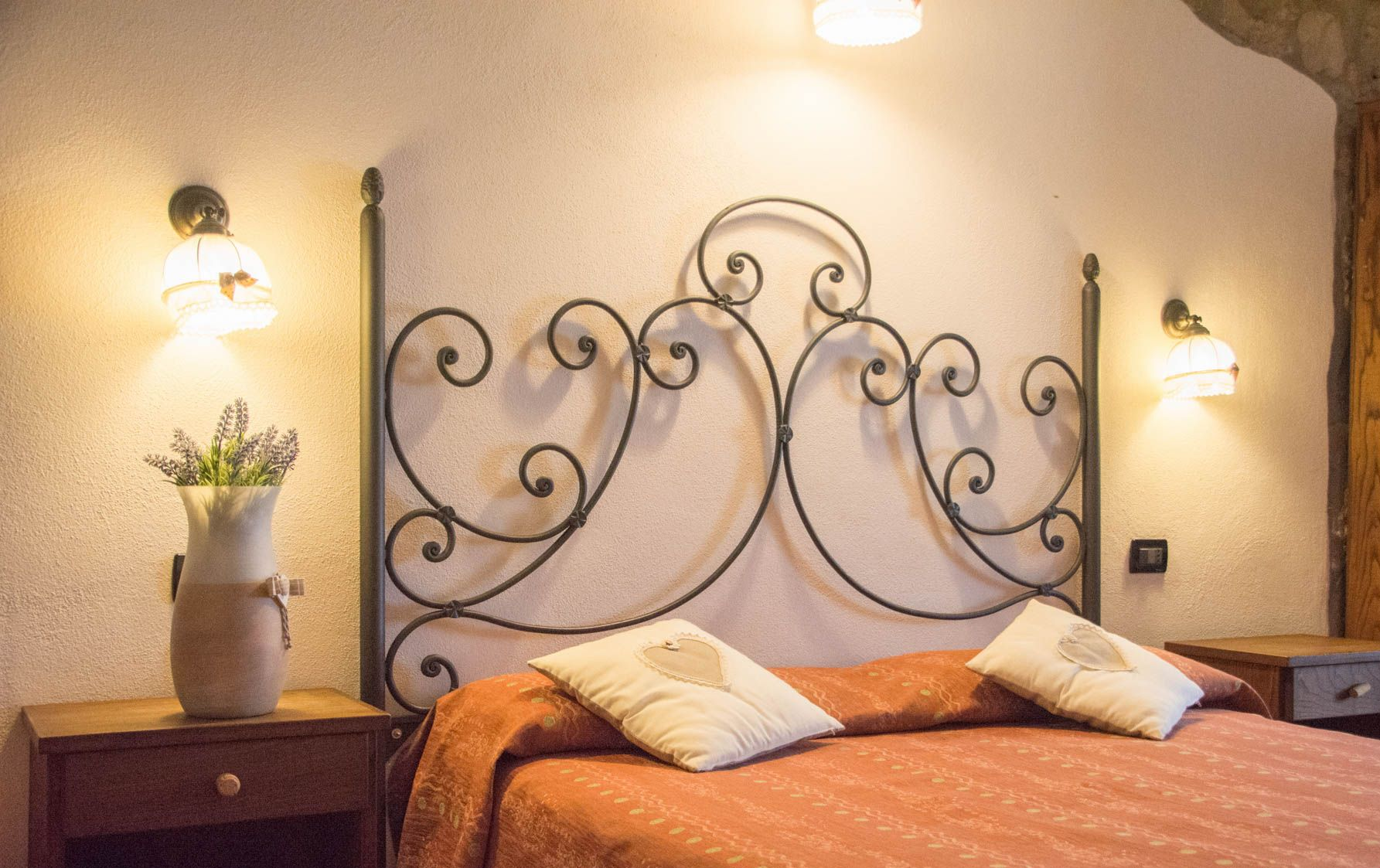 Camera da letto con testiera in ferro battuto, copriletto arancione, lampade da parete e comodini.