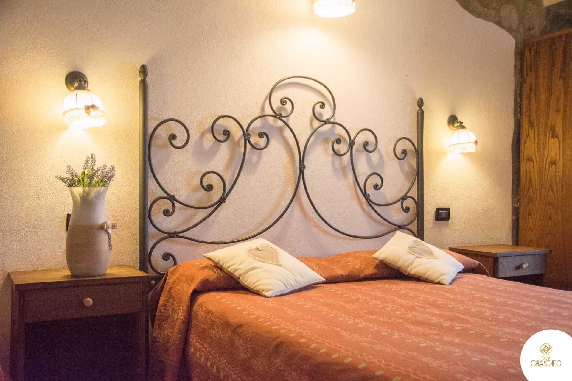 Accogliente camera da letto con testiera in metallo nero decorata, copriletto arancione, lampade da comodino e decorazioni murali.