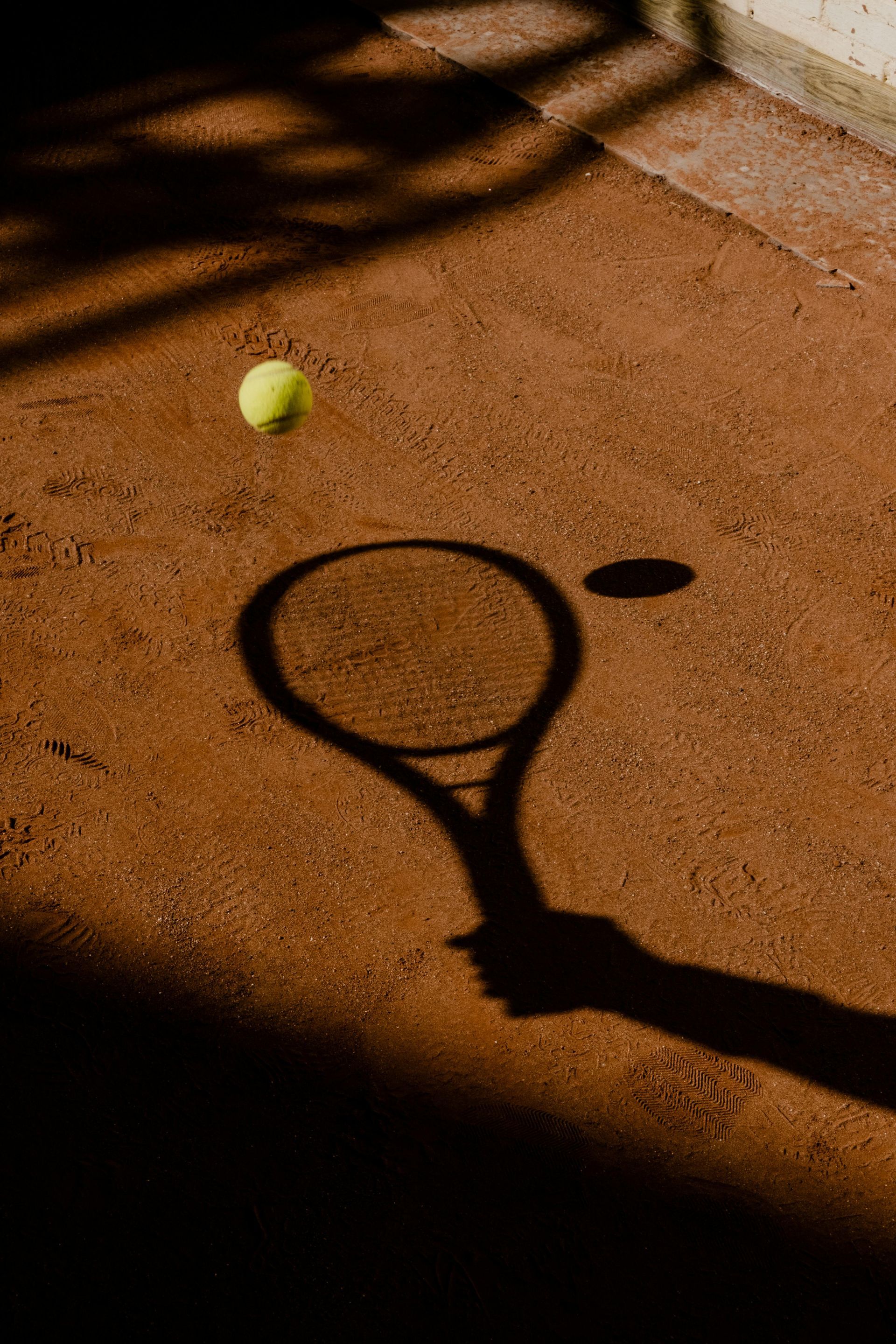 L'ombra di una pallina da tennis e di una racchetta su un campo in terra battuta sotto un caldo sole.