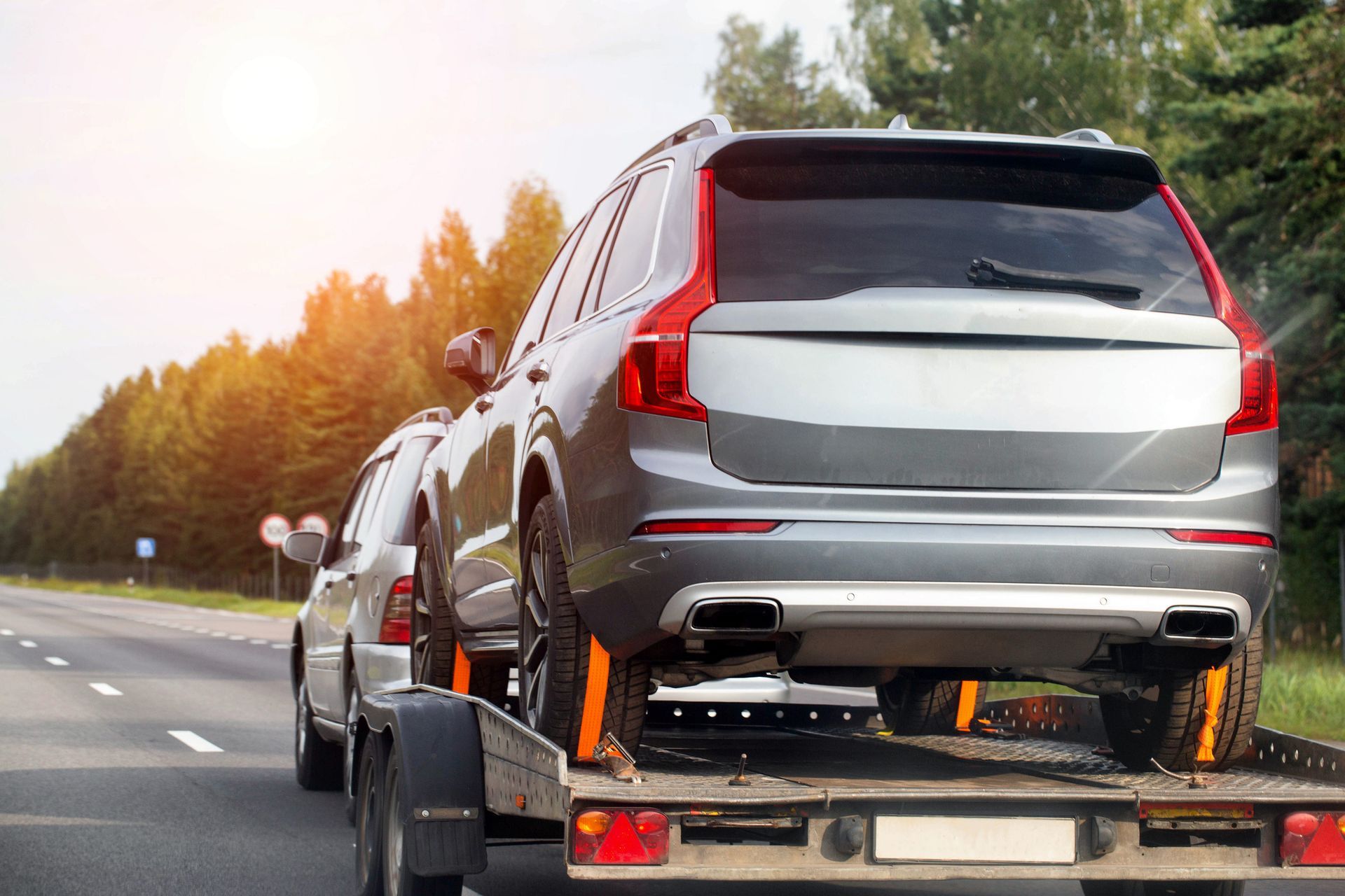 SUV being towed on a flatbed truck, driving on a highway with trees in the background.