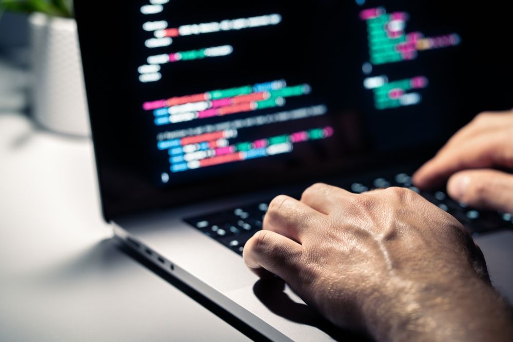 Hands typing code on a laptop keyboard with software displayed on the screen.