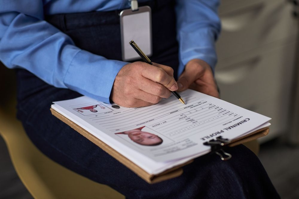 A person in a blue uniform writes on a paper document titled