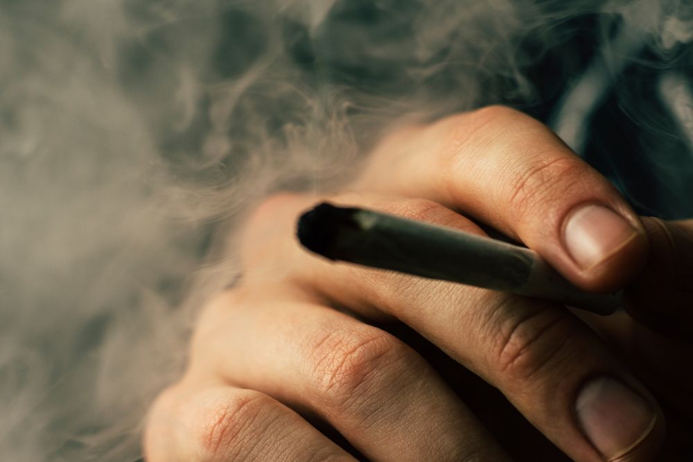 A close-up of a hand holding a lit cigarette surrounded by a dense cloud of smoke.