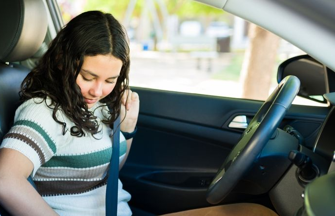 A person sitting in the driver's seat of a car, looking down while fastening their seatbelt.