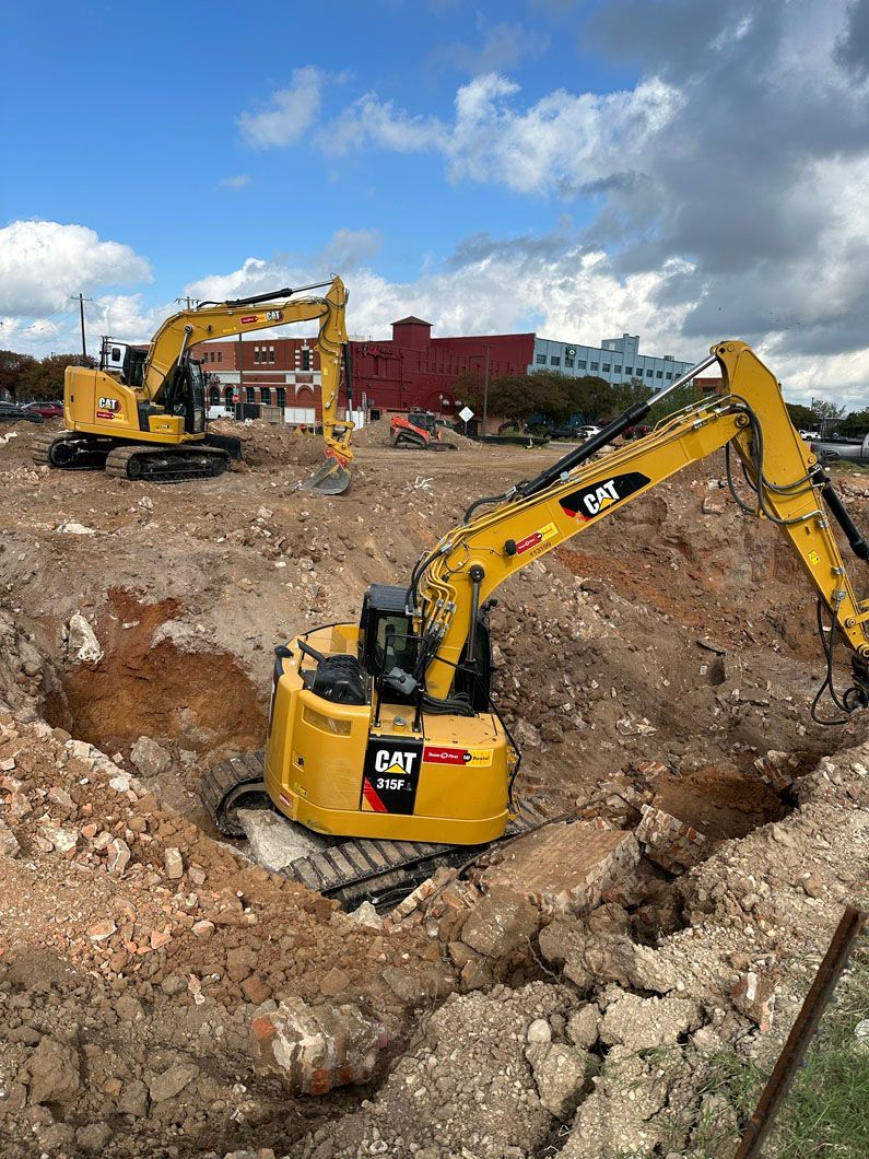Two yellow excavators are digging a hole in the dirt on a construction site.