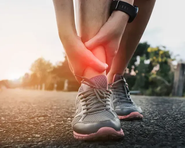 Runner holding ankle in pain, red glow indicating injury; outdoors on pavement.
