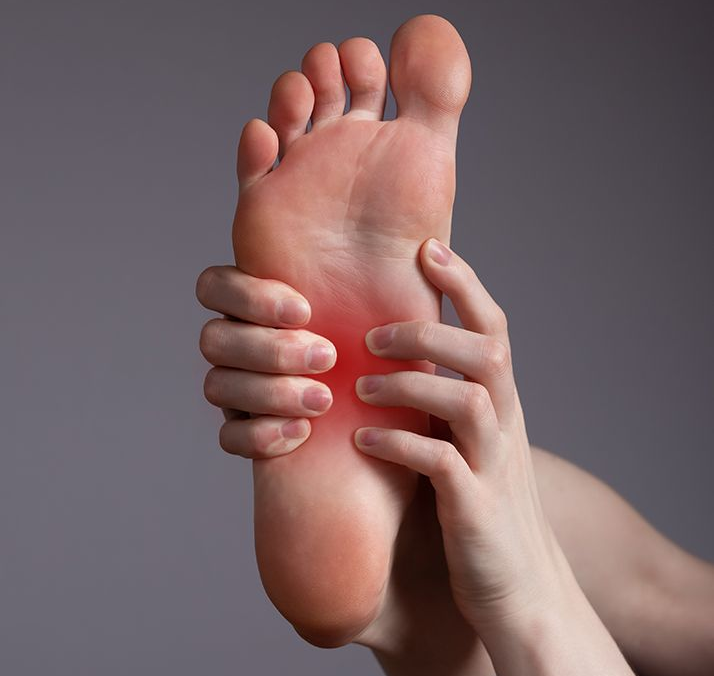 A person holding foot with red pain highlight on the arch, against gray background.