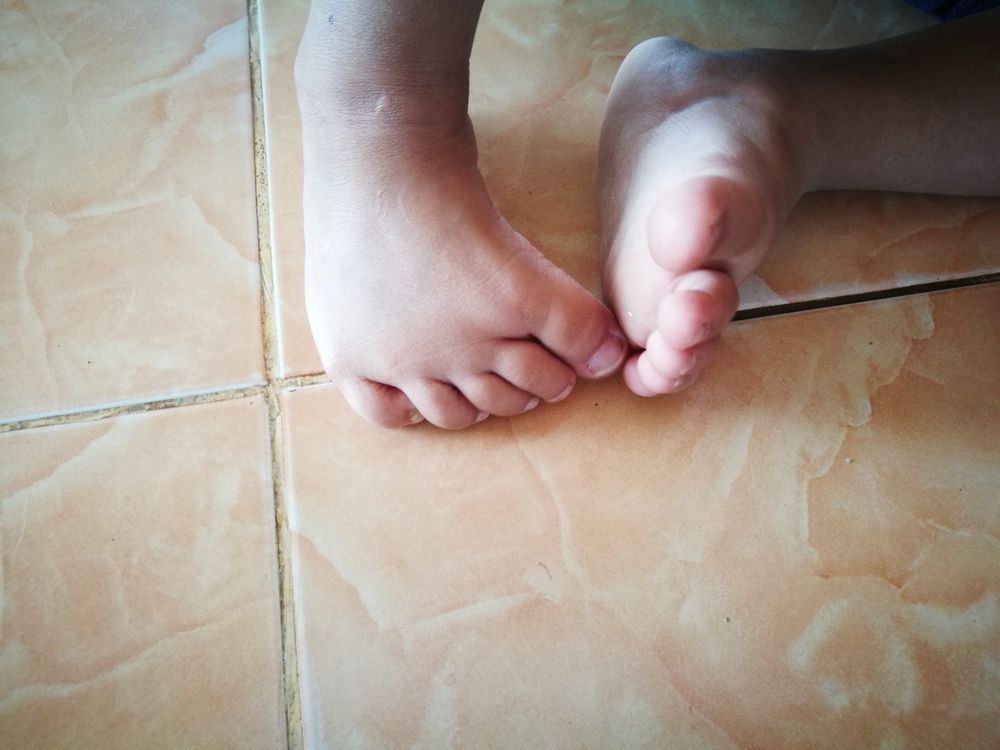 Bare feet resting on a light brown tiled floor.