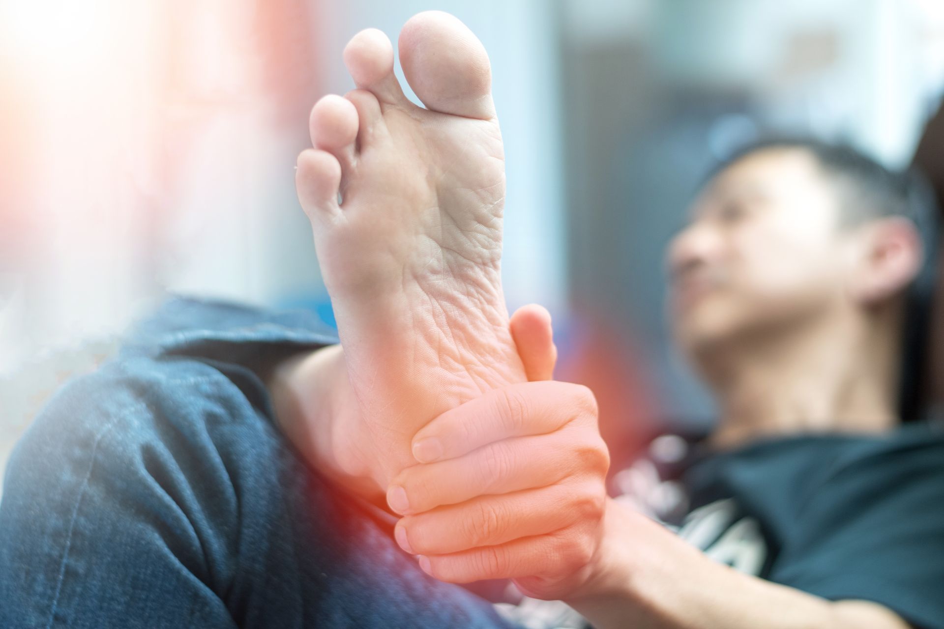 Man holding his foot, which is highlighted in red, suggesting pain.