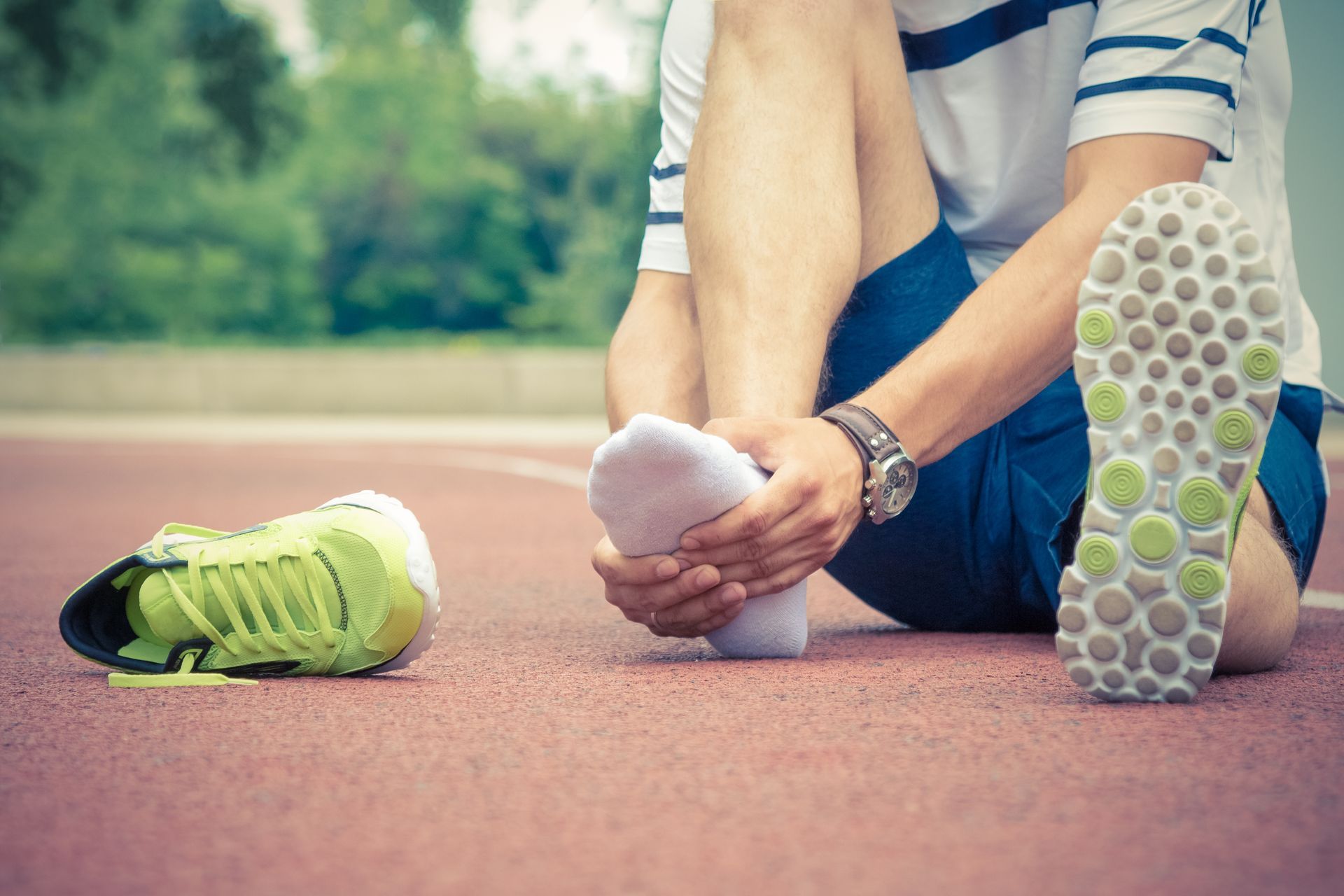 Man seated on a track, holding his foot, with a running shoe beside him, possibly injured.
