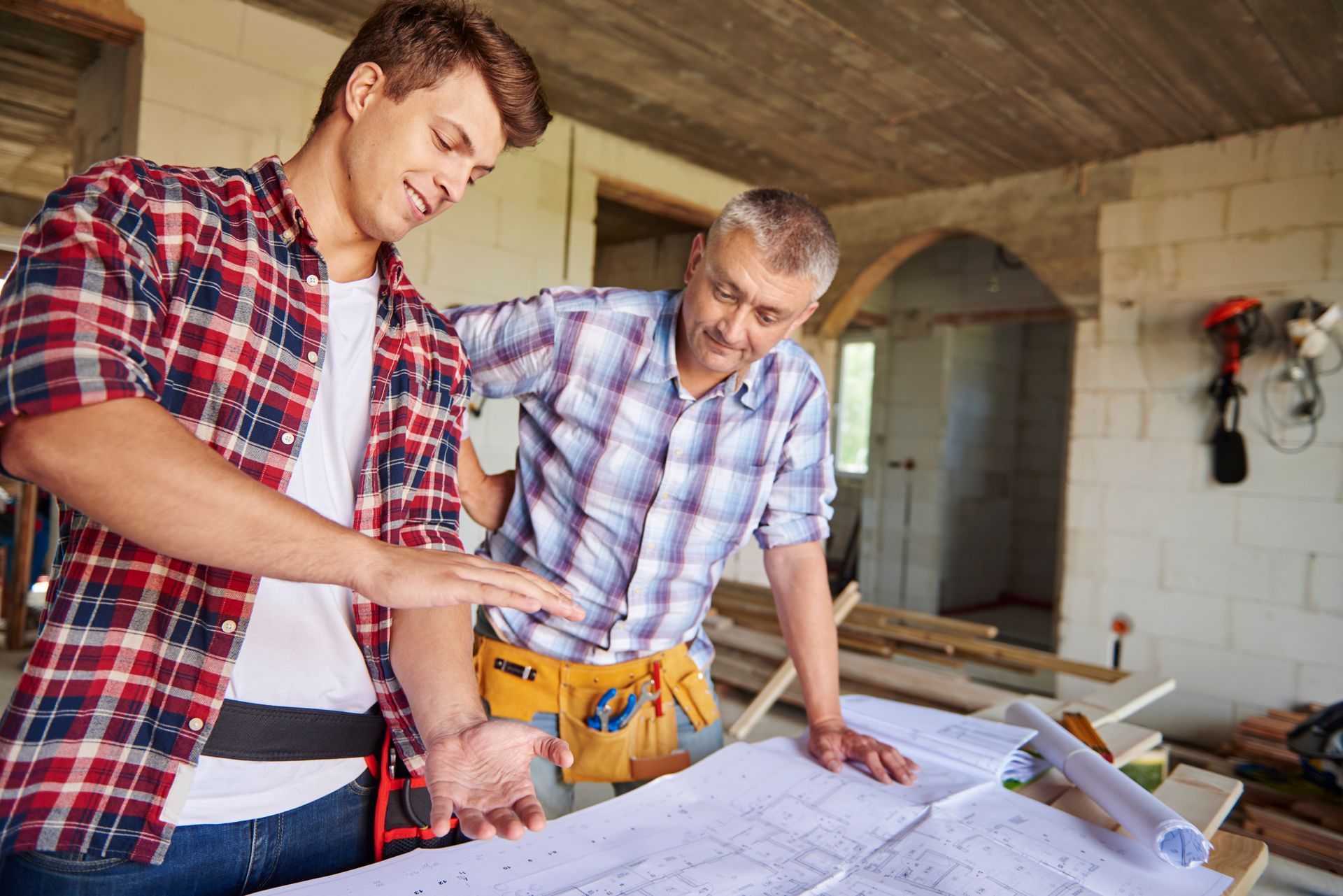 Deux hommes en chemises à carreaux examinent des plans sur un chantier de construction.