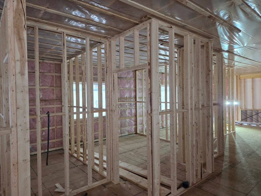 Vue intérieure d'une pièce en construction avec une ossature en bois et une isolation rose.