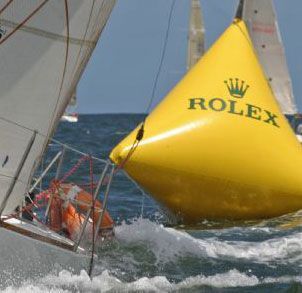 A rolex buoy is being pulled by a sailboat in the ocean.