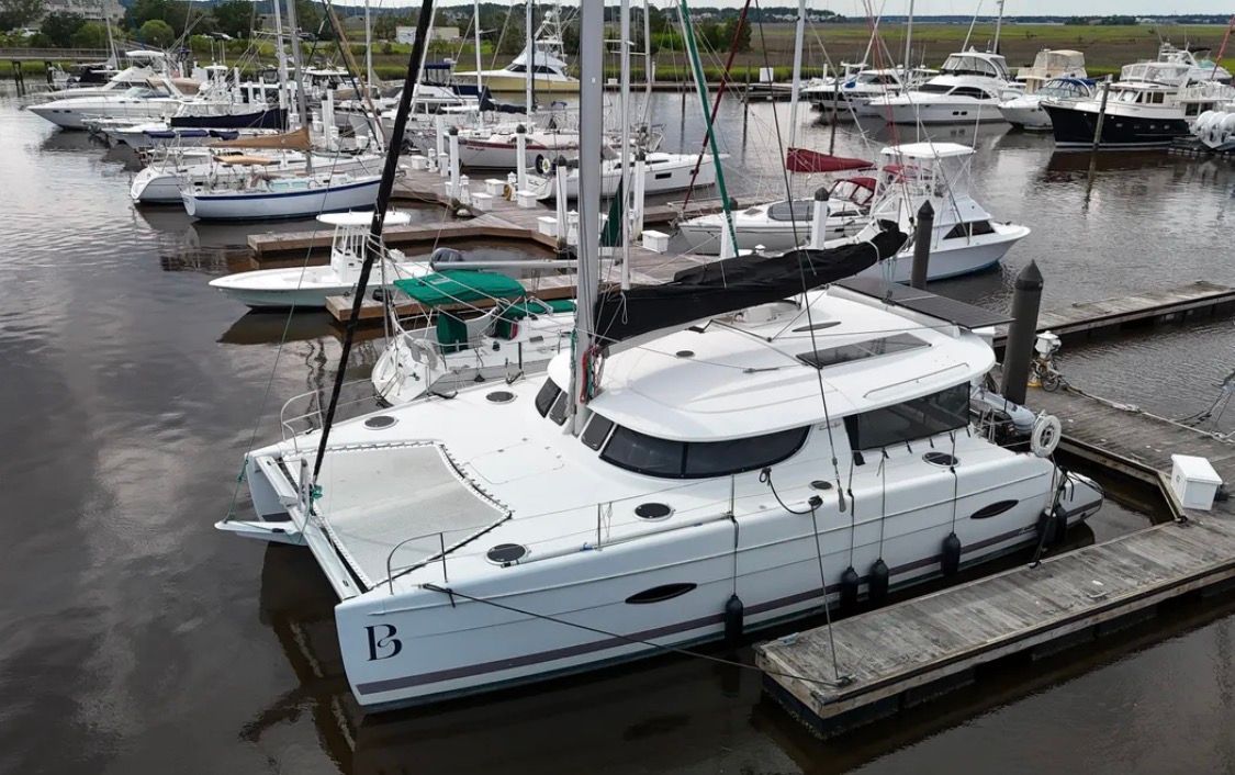 White catamaran docked at a marina with other boats and calm water nearby