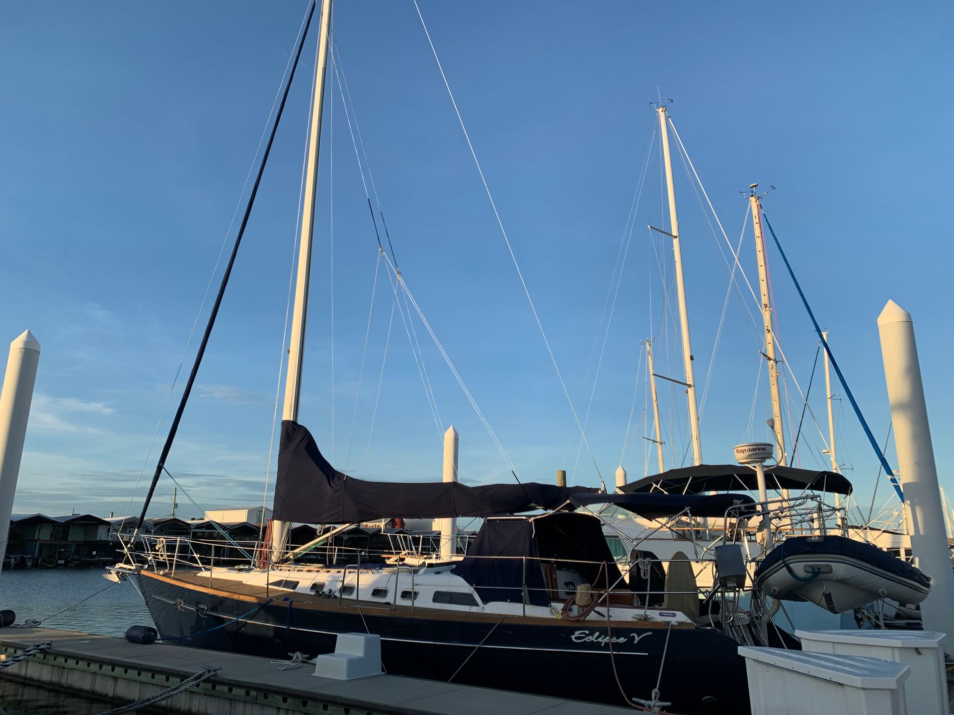 Sailboats docked at a marina at sunset, with tall masts against a clear blue sky.