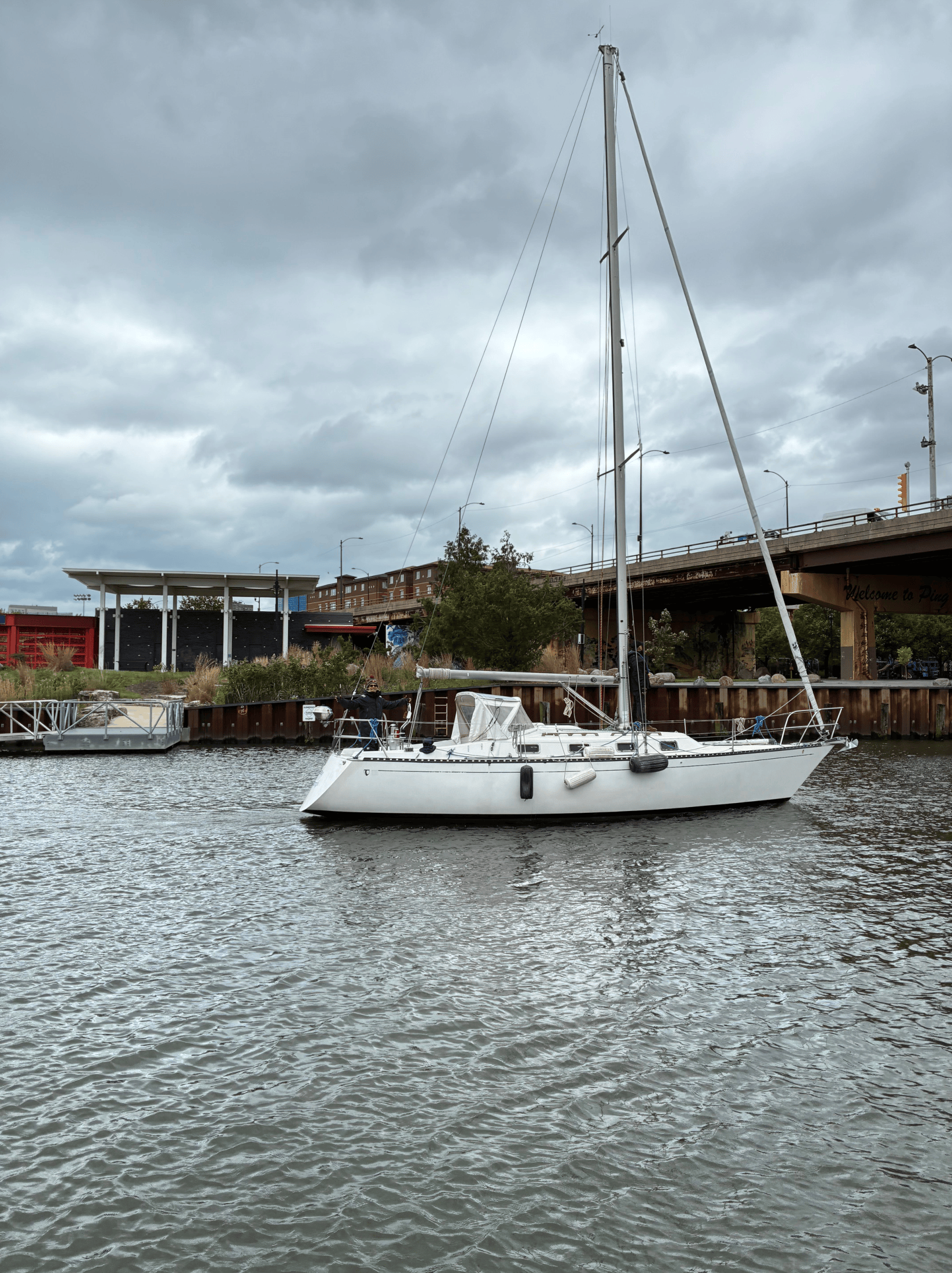 A dark-hulled sailboat with a mast and an American flag docked in calm, bright blue tropical water.
