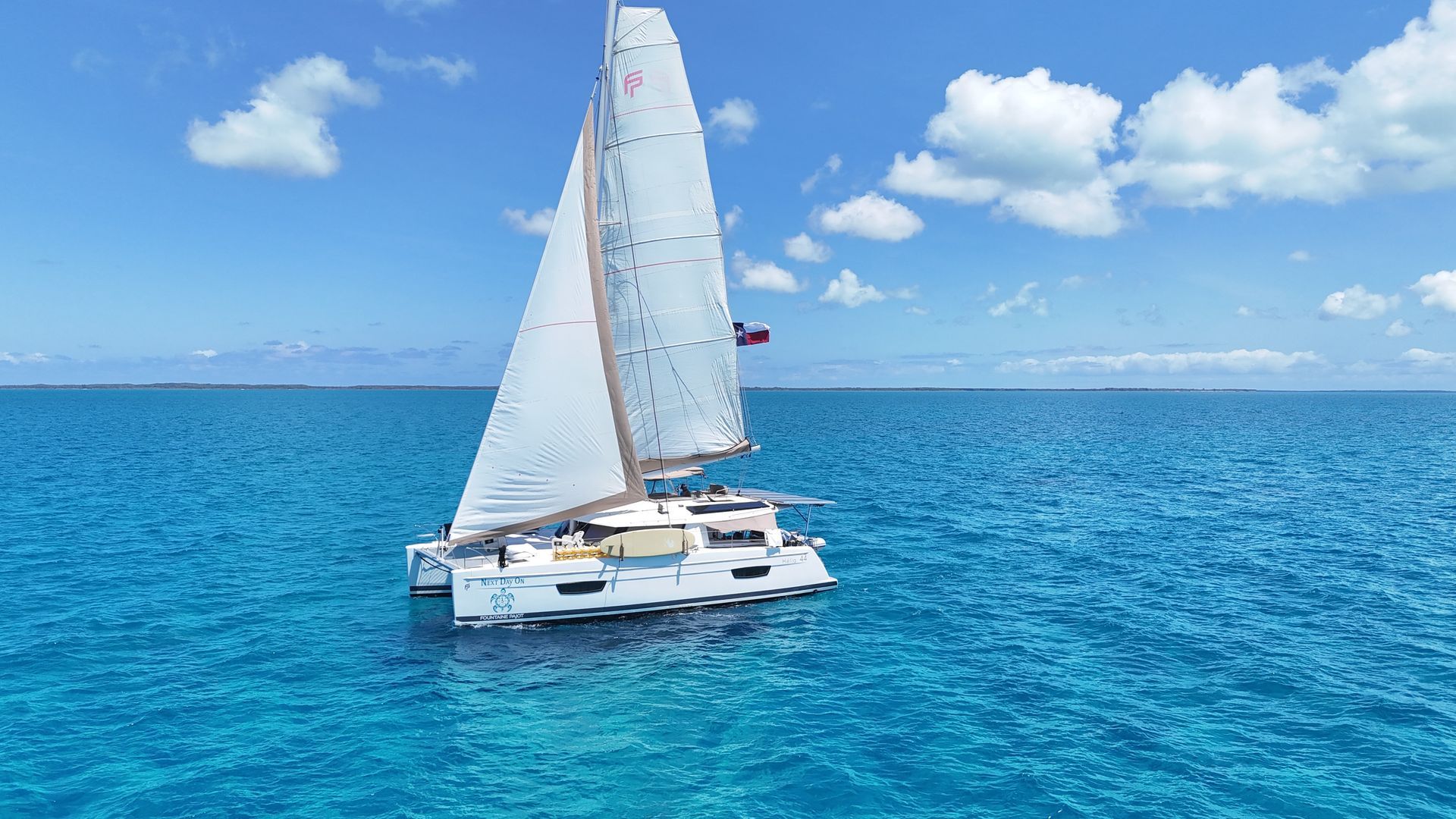 White sailboat on calm water in a marina with palm trees and cloudy sky
